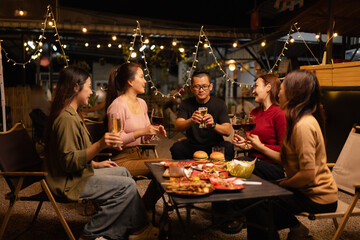 Happy Friends Celebrating Together at Night, Young Asian Group of Friends Having Fun and Toasting Drinks Outdoors, Enjoying a Celebration Concept.