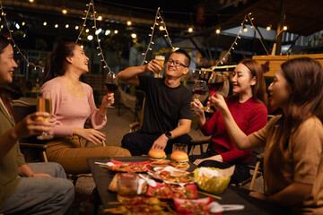 Happy Friends Celebrating Together at Night, Young Asian Group of Friends Having Fun and Toasting Drinks Outdoors, Enjoying a Celebration Concept.