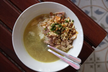 Chicken soto in a white bowl on a wooden table. Indonesian food. soto ayam Kediri. turmeric chicken clear soup.