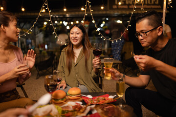 Happy Friends Celebrating Together at Night, Young Asian Group of Friends Having Fun and Toasting Drinks Outdoors, Enjoying a Celebration Concept.