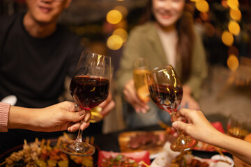 Concept for friendship, celebration, and lifestyle. A group of friends making a toast with various drinks wine, beer, and spirits during an outdoor night gathering.