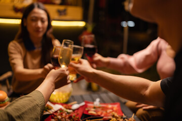Concept for friendship, celebration, and lifestyle. A group of friends making a toast with various drinks wine, beer, and spirits during an outdoor night gathering.