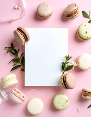 Blank card surrounded by pastel macarons and greenery on pink background