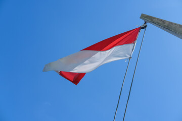 Indonesian flag waving proudly on a tall wooden pole against a clear blue sky, symbolizing independence, unity, and national pride with its red and white colors standing out brightly.