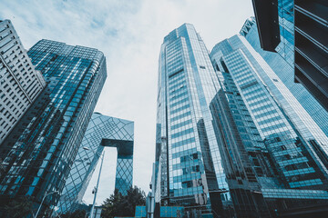 Fototapeta premium Reflective skyscrapers dominate Beijing's CBD skyline, showcasing geometric patterns and a glossy, modern architectural design under a bright, sunny day.