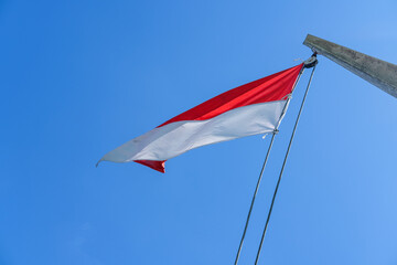 Indonesian flag waving proudly on a tall wooden pole against a clear blue sky, symbolizing independence, unity, and national pride with its red and white colors standing out brightly.