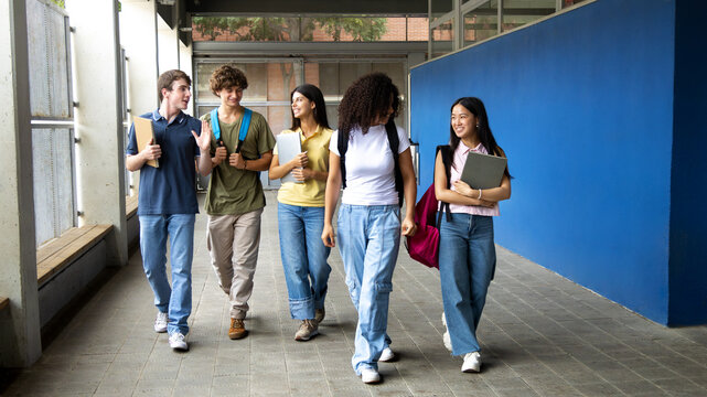 Happy students walking and talking at school corridor
