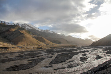 Mountainous landscape with rocky riverbed under cloudy sky