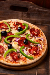 Pizza with chorizo ​​sausage, mozzarella cheese, green pepper and black olives. Rustic wooden background. Soft focus.	