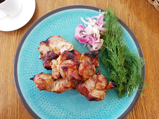 Pork shashlik with onions in a plate on a wooden table in a restaurant