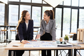 Two businesswomen discussing work using digital tablet and laptop in modern office, Business team analyzing financial data on a digital tablet and paper report.