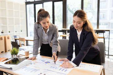 Two businesswomen discussing work using digital tablet and laptop in modern office, Business team analyzing financial data on a digital tablet and paper report.