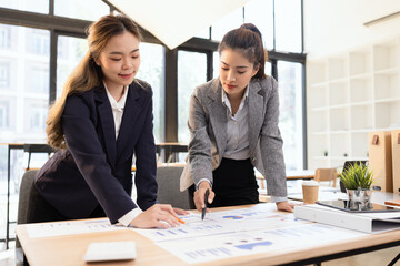 Two businesswomen discussing work using digital tablet and laptop in modern office, Business team analyzing financial data on a digital tablet and paper report.
