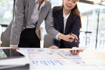 Two businesswomen discussing work using digital tablet and laptop in modern office, Business team analyzing financial data on a digital tablet and paper report.