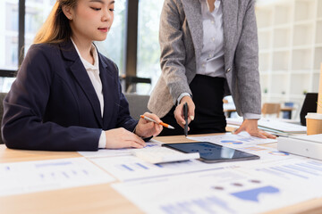 Two businesswomen discussing work using digital tablet and laptop in modern office, Business team analyzing financial data on a digital tablet and paper report.