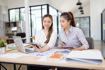 Two businesswomen discussing work using digital tablet and laptop in modern office, Business team analyzing financial data on a digital tablet and paper report.
