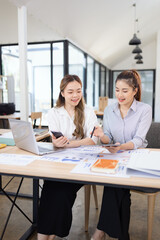Two businesswomen discussing work using digital tablet and laptop in modern office, Business team analyzing financial data on a digital tablet and paper report.