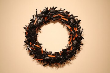 Fototapeta premium A circular wreath, composed of fragmented black and burnt orange strips, displays a dynamic and abstract design against a plain backdrop.