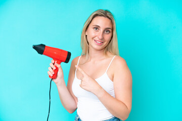 Young caucasian woman holding a hairdryer isolated on blue background and pointing it