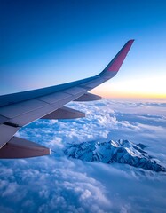 Obraz premium Airplane wing over clouds and mountains at sunrise