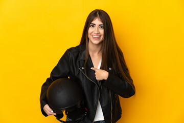 Young caucasian woman holding a motorcycle helmet isolated on yellow background with surprise...