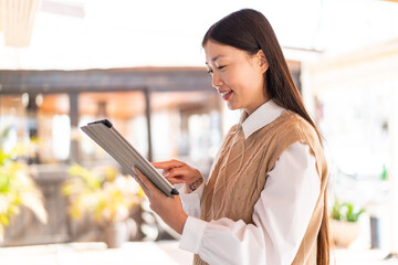 Young Chinese woman at outdoors touching the tablet screen with happy expression