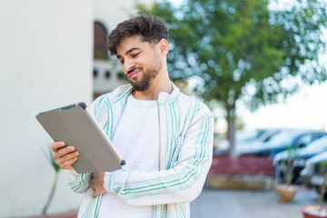 Handsome Arab man holding a tablet at outdoors with sad expression