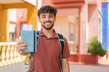 Young Arabian handsome man holding a passport at outdoors with happy expression