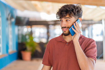 Young Arabian handsome man at outdoors keeping a conversation with the mobile phone with someone