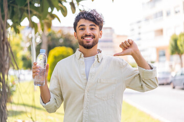 Young Arabian handsome man with a bottle of water at outdoors proud and self-satisfied