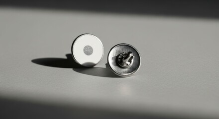 Two round, metallic, decorative buttons.  One plain white, one textured