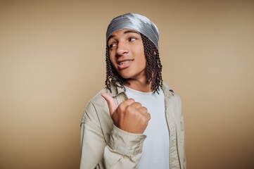 Young man with braided hair wearing a durag, pointing thumb