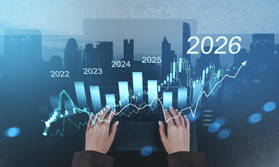Hands typing on laptop with futuristic financial chart showing growth from 2022 to 2026 over cityscape, symbolizing data analytics and future trends.