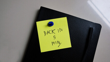 Back in 5 min message concept written post it on notebook.