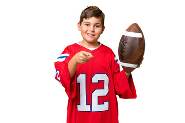 Little caucasian kid playing rugby over isolated chroma key background points finger at you with a...