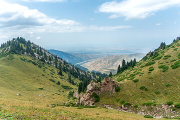 A panoramic view from a mountain slope shows a dormant stream gorge with rocky outcrops leading...