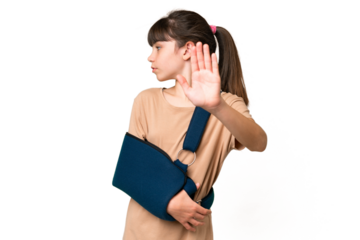 Little caucasian girl with broken arm and wearing a sling over isolated background making stop gesture and disappointed
