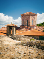 Exterior view of a historic Eastern Orthodox monastery built from stone with traditional Byzantine-style architecture, terracotta roof tiles, wooden stairways and large ceramic pots with plants