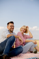 Happy couple enjoying a sunny day on a picnic blanket in a golden field, laughing and sharing joyful moments together