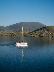A small sailing boat gliding through calm blue waters near the Greek islands during a warm summer evening. The peaceful scene captures the essence of Mediterranean travel, island hopping, and relaxed