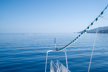 View from the bow of a boat decorated with string lights over the calm blue waters of the Aegean Sea in Greece.  Perfect image to capture the essence of sailing, slow travel, 