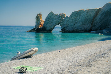 Scenic view of the famous Lalaria Beach on the island of Skiathos, Greece. A striking natural stone arch rises from the turquoise Aegean Sea, with white pebble shore in the foreground.