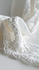 Delicate white lace fabric draped on a white background, showcasing its intricate floral pattern and texture