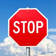 Obraz premium Red octagonal stop sign against a bright blue sky and fluffy white clouds