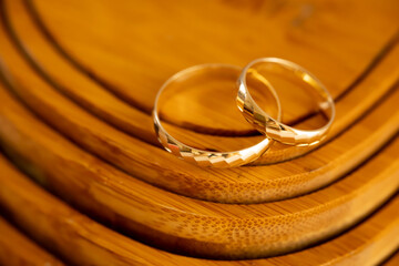macro photo of wedding gold rings on a textured wooden background in warm tones, macro of wedding rings on light brown wood