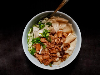 Overhead view of savory Wonton Noodles with braised meat and chopped scallions in a ceramic bowl