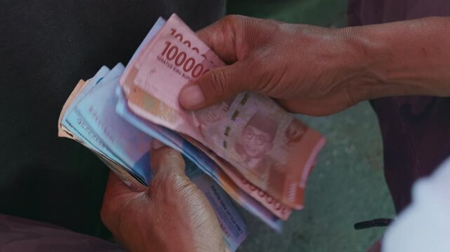 Close-up of workers&rsquo; hands holding and counting Indonesian rupiah banknotes, shifting the money between fingers.