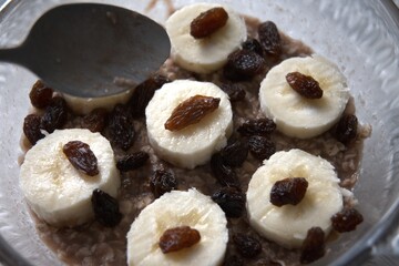 Healthy breakfast of chocolate oatmeal topped with banana slices and raisins in close-up view.