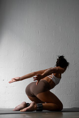 Fototapeta premium Athletic woman performing dynamic seated twist on yoga mat, arms extended gracefully, wearing brown shorts and a white sports bra, showcasing strength, flexibility, and control during workout 