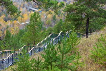 Metal stairway on hill slope among the green pines in autumn day. The longest staircase in Russia on the Torgashinsky Ridge in Krasnoyarsk, Russia